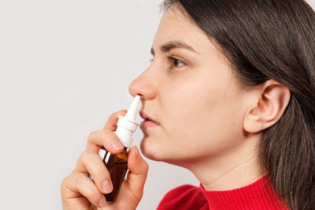 Девушка в красном свитере капает лекарство в нос