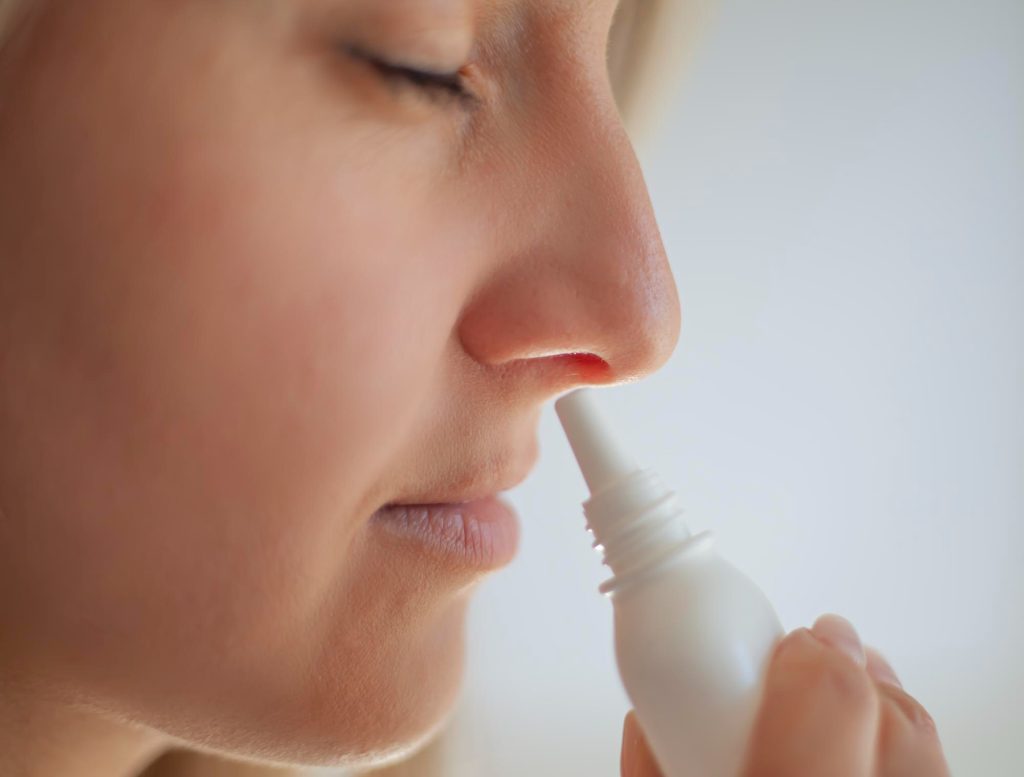 Женщина подносит к ноздре пузырек с назальным спреем